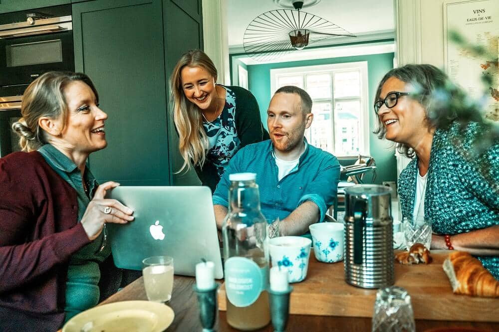 familie der sidder sammen. Kvinde fortæller om sit nye job og om at hun har ændret sine forsikringer så de passer.